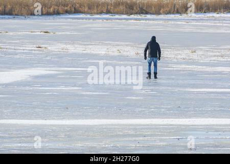 Mann von hinten, der auf dem Eis eines gefrorenen Sees steht, fröhliche Winteraktivitäten oder gefährliche Kühnheit bei auftauendem Wetter, Kopierraum, ausgewählter Fokus Stockfoto