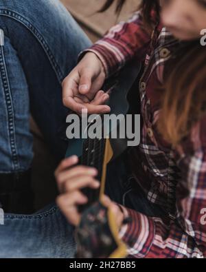 Junge Frau, die im Herbstwald Ukulele-Gitarre spielt Stockfoto