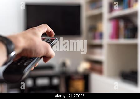 Mann wechselt die Sender auf einem Plasma-Fernseher mit Fernbedienung zu Hause Stockfoto