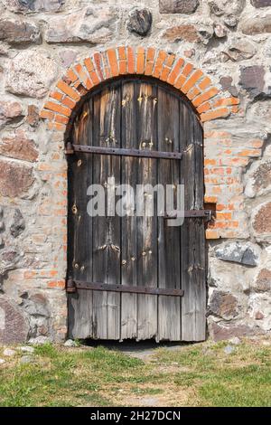 Alte gewölbte Holztür in einer Steinwand, vertikale Hintergrund Foto Textur Stockfoto