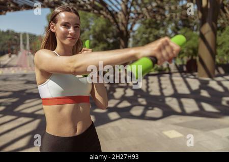 Positive Frau macht Sportübungen mit Kurzhanteln im grünen Stadtpark Stockfoto