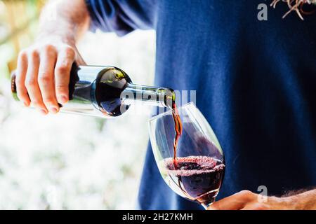 Ein junger Mann mit einer Flasche, der Wein in ein Glas gießt. Stockfoto