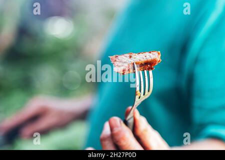 Mann, der ein Stück Fleisch mit einer Gabel gebraten anbietet. Stockfoto