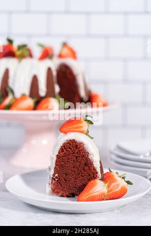 Ein Stück roter Samtkuchen mit Frischkäse-Zuckerguss, garniert mit frischen Erdbeeren auf einem weißen Teller. Stockfoto