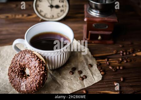 Ein Glas Kaffee auf dem Tisch mit Uhr am Morgen. Ein Vintage-Wecker, der 9:00 Uhr auf dem Tisch neben einer Tasse Kaffee und einem Donut anzeigt. Frühstück. Zeit m Stockfoto