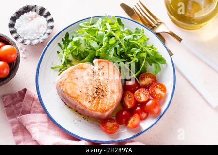 Gebratenes Thunfischsteak mit Rucola und Kirschtomaten, Gourmet-Menü auf einem rosafarbenen Teller Stockfoto