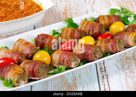 Fleischbällchen in Speckverpackung mit Tomaten und kühlem Souce auf weißem Teller Stockfoto