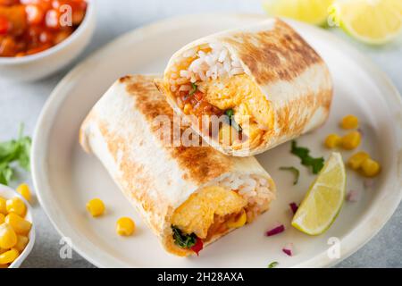 Frühstückstortilla Wrap mit Omelette und Gemüse auf einem Teller. Gesunder vegetarischer Burrito mit Eiern Stockfoto