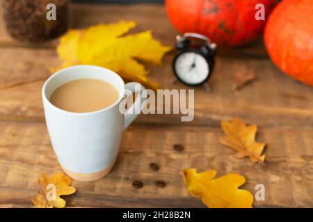 Aromatisierter Kürbiskaffee mit Gewürzen in einer keramischen Tasse auf einem Holztisch mit orangefarbenen Kürbissen und trockenen Blättern im Hintergrund. Herbststimmung. Zeit für dri Stockfoto