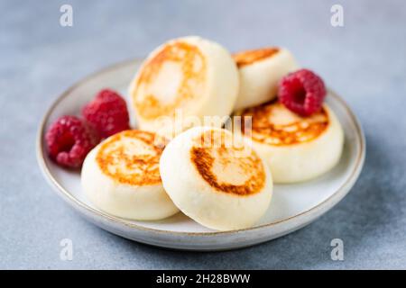 Hüttenkäse-Krapfen mit Himbeeren isoliert auf blauem Beton-Hintergrund, Nahaufnahme Stockfoto