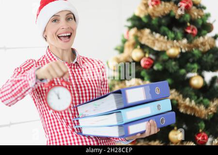 Porträt einer jungen lächelnden Frau im weihnachtsmannhut halten Wecker und Geschäftsunterlagen auf dem Hintergrund Stockfoto