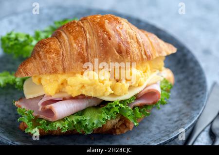Croissant-Sandwich mit Ei und Schinken auf einem Teller, Nahaufnahme. Leckeres Sandwich Stockfoto