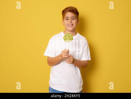 Kleiner Junge mit buntem Lollipop isoliert auf gelbem Hintergrund Stockfoto