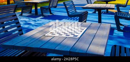Selektiver Fokus auf ein leeres Schachbrett auf dem Tisch im Freien. Schachtische auf blauem Boden in einem Stadtpark an einem sonnigen Tag. Brettspiele im Stadtpark unter freiem Himmel. Stockfoto