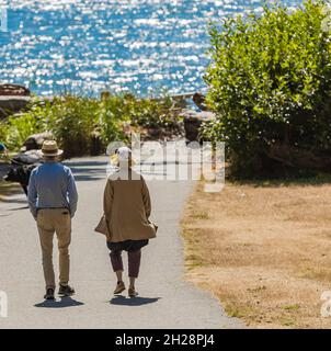 Rückansicht eines aktiven älteren Ehepaares, das auf der Parkstraße entlang der Küste im Freien läuft. Stockfoto