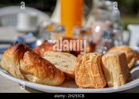 ARGENTINISCHES FRÜHSTÜCK IM GARTEN. KEKSE, CROISSANTS, ORANGENSAFT, MILCH, KAFFEE. HORIZONTAL. SELEKTIVER FOKUS Stockfoto