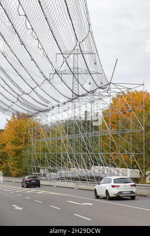 Ein großes Gerüst mit Sicherheitsnetz zum Schutz des Straßenverkehrs aufgrund von Arbeiten an einer Hochspannungsleitung und den Strommasten. Stockfoto