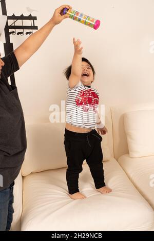 2-jähriger Kleinkind Junge lachend, als er nach Spielzeug greift Elternteil hält aus seiner Reichweite Stockfoto