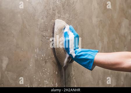 Nahaufnahme Hand tragen blaue Gummihandschuhe ist mit einem Schwamm Reinigung an der Betonwand. Stockfoto