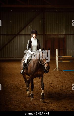 Junge Reiterin auf Dressurpferd. Eine abstrakte Aufnahme des Pferdes während des Wettkampfs. Nettes Mädchen Jockey sitzt im Sattel auf einem Pferd, aktiven Lebensstil. Stockfoto