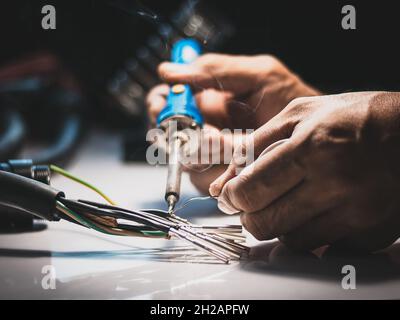 Elektriker verwenden einen Lötkolben, um die Drähte mit dem Metallstift mit Lötkabel zu verbinden. Stockfoto