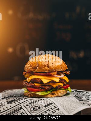 Köstlicher Burger mit Salat, Käse, Gurken, Zwiebeln und Tomaten auf dunklem Hintergrund AUS NÄCHSTER NÄHE Stockfoto
