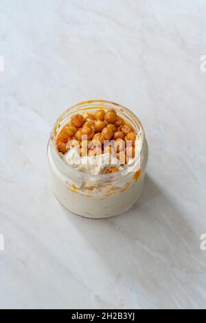 Hummus mit knusprigem Chickpeasi-Olivenöl, Paprika und Zitrone in Glasschüssel zum Mitnehmen. Bereit zum Essen. Stockfoto