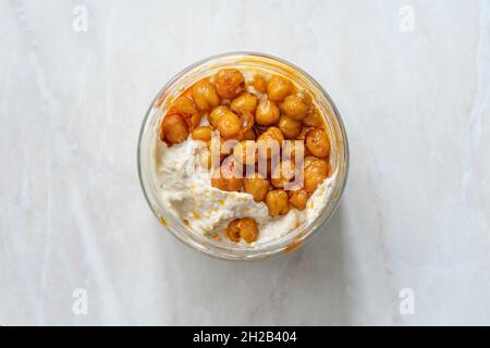 Hummus mit knusprigem Chickpeasi-Olivenöl, Paprika und Zitrone in Glasschüssel zum Mitnehmen. Bereit zum Essen. Stockfoto