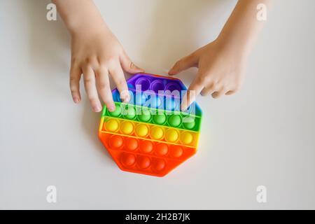 Legen Sie es zappelig in die Hände der Kinder. Bunte Spielzeug Push Pop it. Draufsicht auf die sensorische Antistress-Fidget-Spannung. Stockfoto