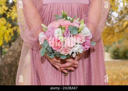 Die Braut in einem rosa Kleid hält einen Strauß rosa-weißer Rosen in der Herbstpark-Nahaufnahme. Stockfoto