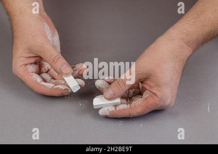 Zwei Hände eines erwachsenen Mannes, der weiße Kreide auf einem grauen Hintergrund hält. Selektiver Fokus. Stockfoto