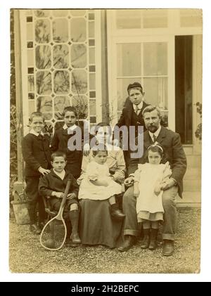 Originales edwardianisches Foto einer großen, attraktiven Familie, 6 Kinder, meist Jungen, die vor einem großen Haus sitzen. Die Mutter hat ein Baby oder Kleinkind auf dem Schoß, das in Mädchenkleidung gekleidet ist, aber ein Junge sein könnte, da kleine Kinder zu diesem Zeitpunkt gleich gekleidet waren. Wohlhabende Reiche sind gut für eine Familie. Großbritannien ca. 1908, Großbritannien Stockfoto