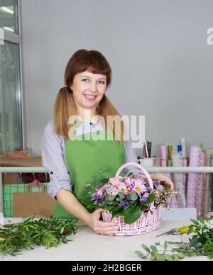 Porträt einer glücklichen lächelnden Floristin, die einen Blumenstrauß in einem Blumengeschäft im Korb hält. Business-, Verkaufs- oder Blumendesign-Konzept. Stockfoto