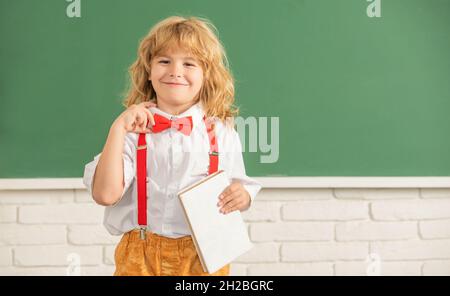 Lächelndes Kind mit Buch. Jugendlicher Junge im Klassenzimmer. Zurück zur Schule. Wissenstag. Stockfoto