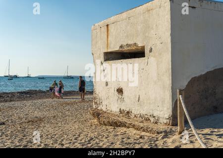 Es Trenc, Spanien; 11 2021. oktober: Alter Bunker des spanischen Bürgerkrieges am Strand von Es Trenc, neben Badegästen, bei Sonnenuntergang. Insel Mallorca, Spanien Stockfoto