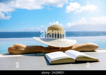 Frau versteckt sich unter Strohhut und ruht im unendlichen Pool. Entspannender Sommerurlaub im Resort Stockfoto