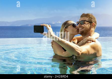Junges Paar in der Liebe unter Selfie im Unendlichen Pool. Romantischer Kurzurlaub, Sommerurlaub Stockfoto