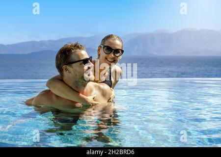 Glücklich lächelndes junges Paar, das Spaß zusammen im Unendlichen Swimmingpool hat. Romantischer Sommerurlaub Stockfoto