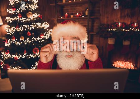 Foto von beeindruckt lustig reifen Mann verkleidet santa Kostüm Arme Brille suchen modernes Gerät drinnen Heim Zimmer Stockfoto