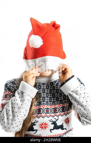 Kinderportrait in weißem Weihnachts-Pullover mit Rentier-Versteck-Gesicht in Weihnachtsmannhut, isoliert auf weißem Hintergrund Stockfoto