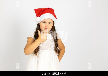 Porträt eines lächelnden, enthusiastischen Kindes in rotem Weihnachtsmannhut gibt Daumen nach oben, isoliert auf weißem Hintergrund mit Kopierraum Stockfoto