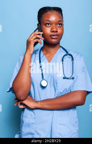 afroamerikanischer Arzt-Assistent im Gespräch am Smartphone Disease Expertise mit Therapeut Kollegen bei der Gesundheitsbehandlung in Studio mit blauem Hintergrund arbeiten diskutieren. Medizinkonzept Stockfoto