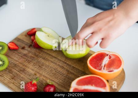 Beschnittene Ansicht einer Frau, die in der Nähe von Grapefruit und Erdbeeren auf dem Schneidebrett einen Apfel schneidet Stockfoto