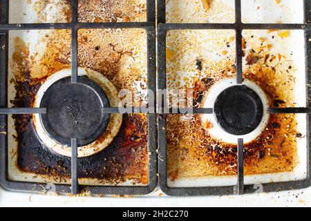 Schmutzige Oberfläche des Gaskofens. Zwei Gasbrenner und ein gusseisernes Gitter eines Gasofens, umgeben von alten Essensresten und Getränken. Oberfläche und Brenner der oberen Fläche Stockfoto