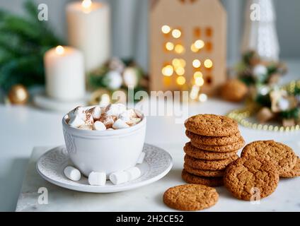 Heißer Kakao mit Moorlachen in weißem Becher, umgeben von winterlicher Weihnachtsdekoration auf weißem Tisch Stockfoto