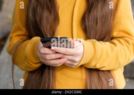 Ein Mädchen mit langen Haaren hält ein Smartphone aus der Nähe. Stockfoto