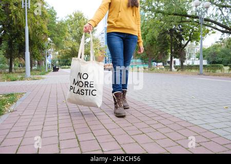 Eine Frau geht die Straße hinunter und hält einen wiederverwendbaren Stoffbeutel, der sagt, kein Plastik mehr. Stockfoto