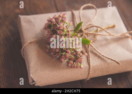 Hausgemachte verpackt in Kraftpapier und rosa Blumen auf einem Holztisch. Nahaufnahme Bild der schönen Geschenkbox mit Blumen geschmückt Stockfoto