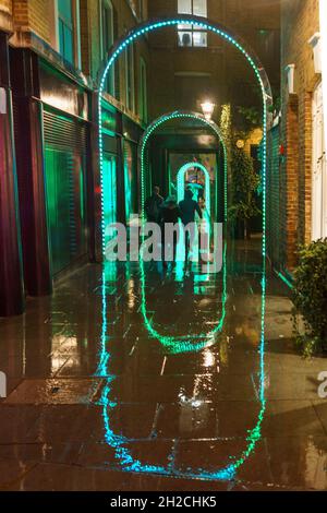 Menschen, die an einem nassen Winterabend in London durch eine beleuchtete Gasse laufen. Stockfoto