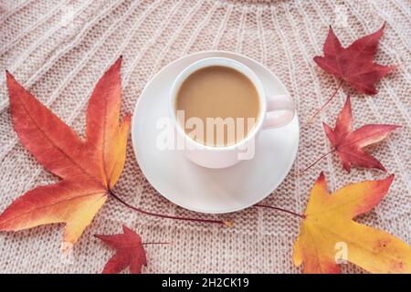 Kaffeetasse und Herbstblätter auf rosa Strickpullover, Draufsicht. Herbstkonzept. Stockfoto